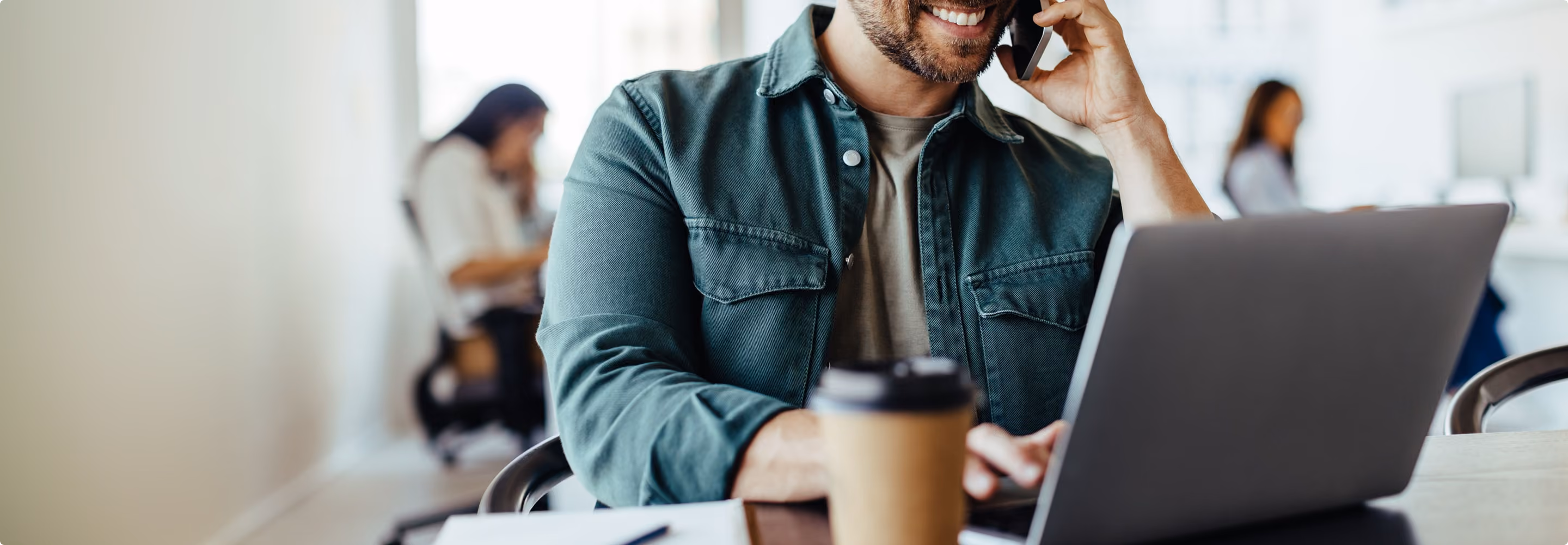 Homem sorridente trabalhando no laptop com café sobre a mesa, pesquisando oportunidades de investimento imobiliário.