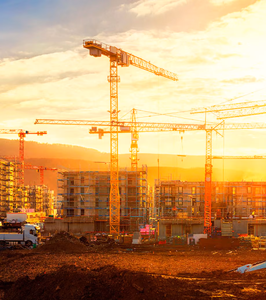 Canteiro de obras ao pôr do sol com guindastes e prédios em construção — etapa de execução de um empreendimento Indepy.