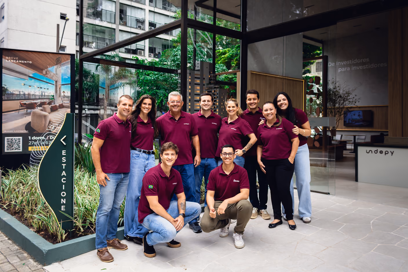 Equipe da Indepy de camiseta vermelha reunida diante de um jardim vertical, representando o ecossistema de incorporação e gestão da empresa em São Paulo.