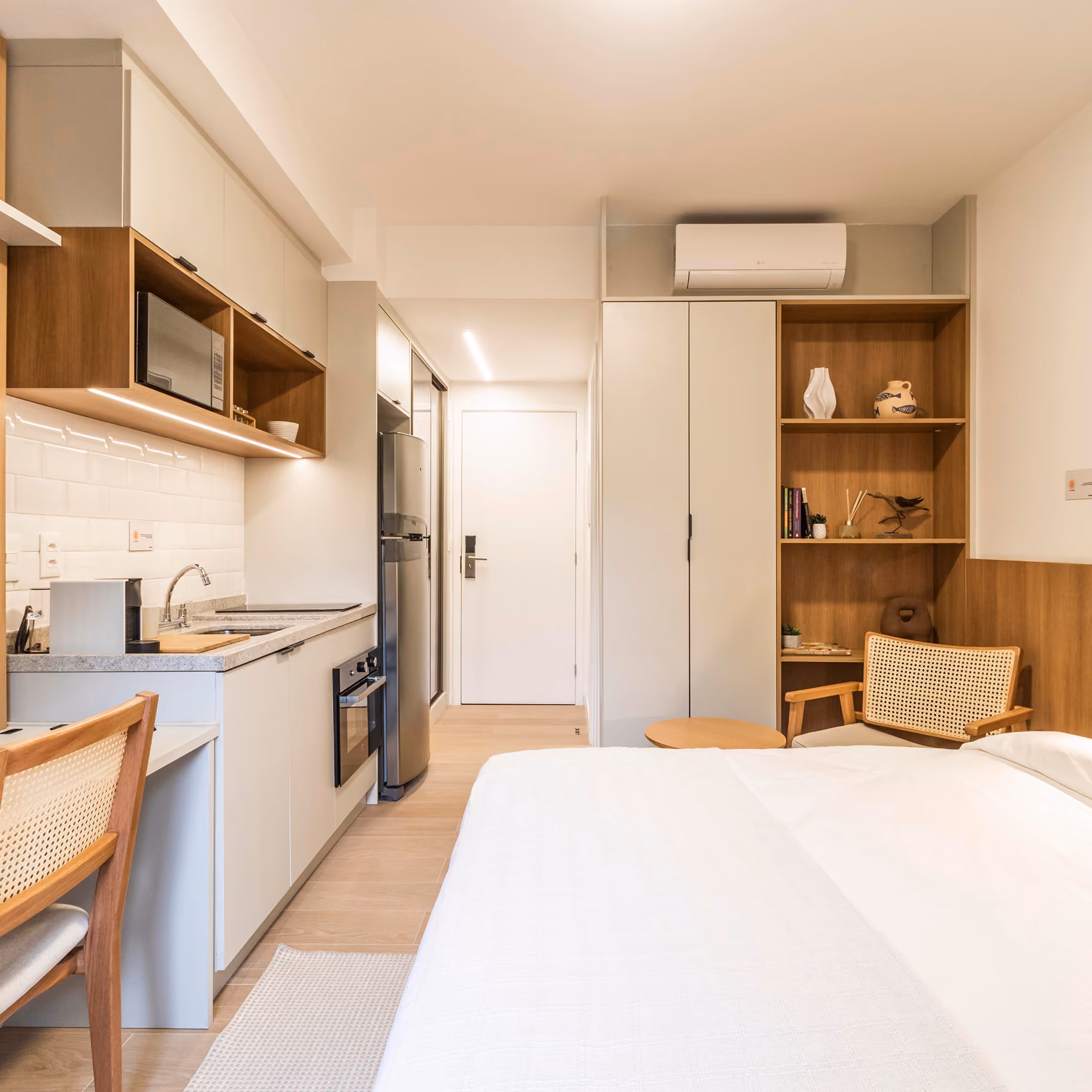 Studio Indepy mobiliado com cozinha integrada, armários em madeira clara, nicho de apoio e cama de casal, formato compacto para locação em São Paulo.