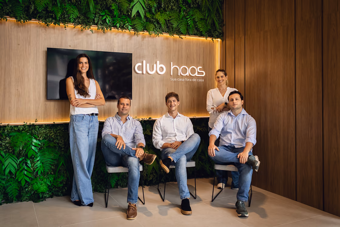 Equipe do Club Haas em frente ao painel com o logotipo da marca e jardim vertical, no lounge da sede que faz a gestão dos empreendimentos Indepy em São Paulo.