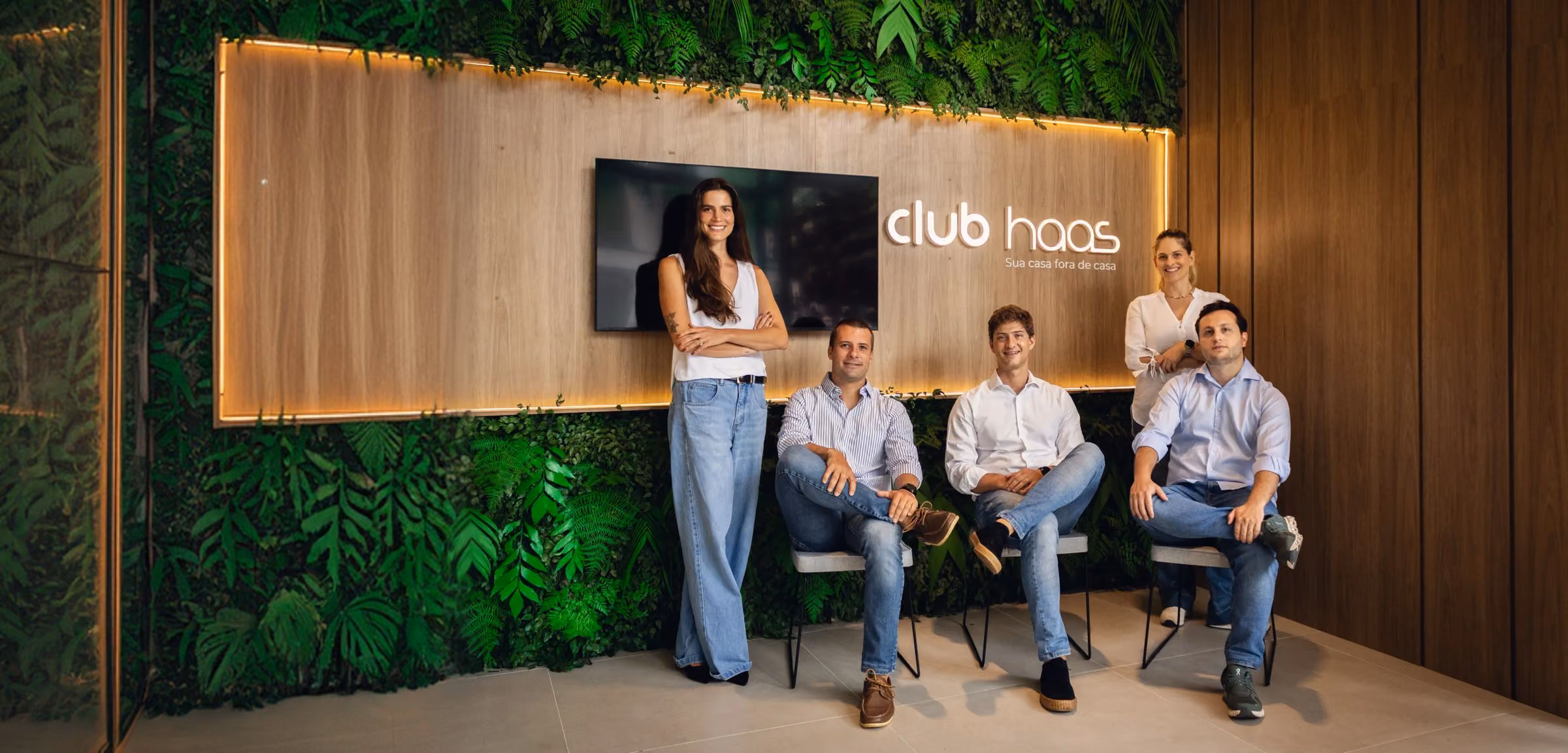 Equipe do Club Haas reunida em frente ao painel com a marca