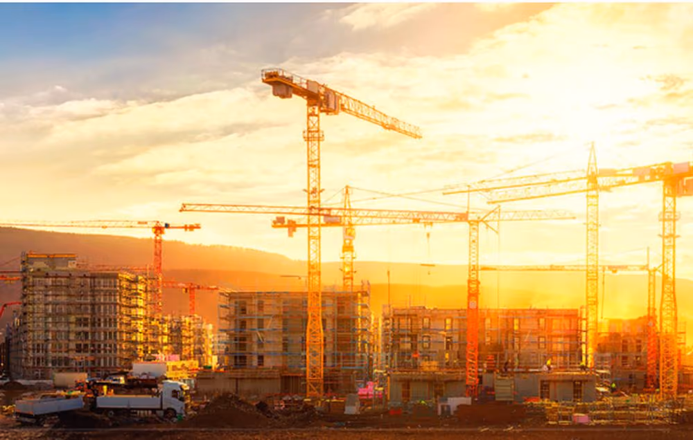 Canteiro de obras ao pôr do sol com guindastes e prédios em construção — fase de lançamento e obra de um empreendimento Indepy.