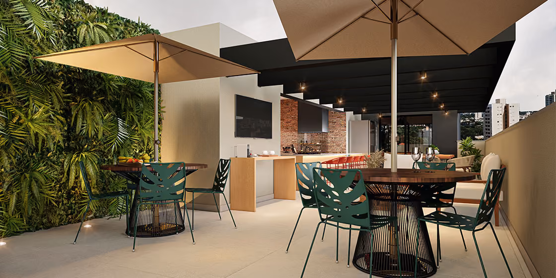 Terraço gourmet de empreendimento Indepy com jardim vertical, guarda-sóis, churrasqueira e mesas altas com cadeiras verdes, área comum de lazer em São Paulo.