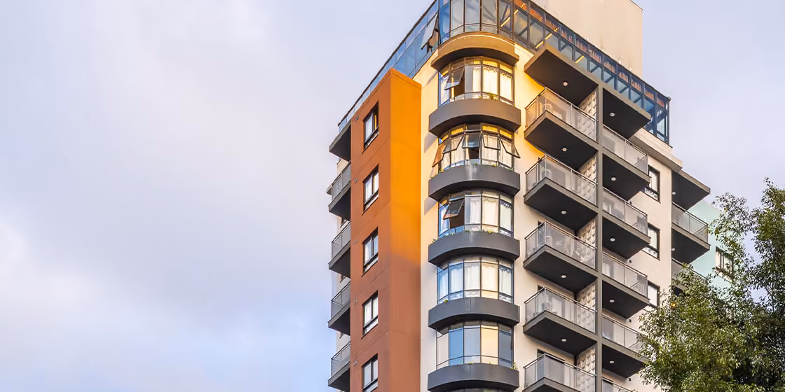 Fachada de empreendimento Indepy ao entardecer, com sacadas curvas envidraçadas e detalhe em laranja na empena, em São Paulo.