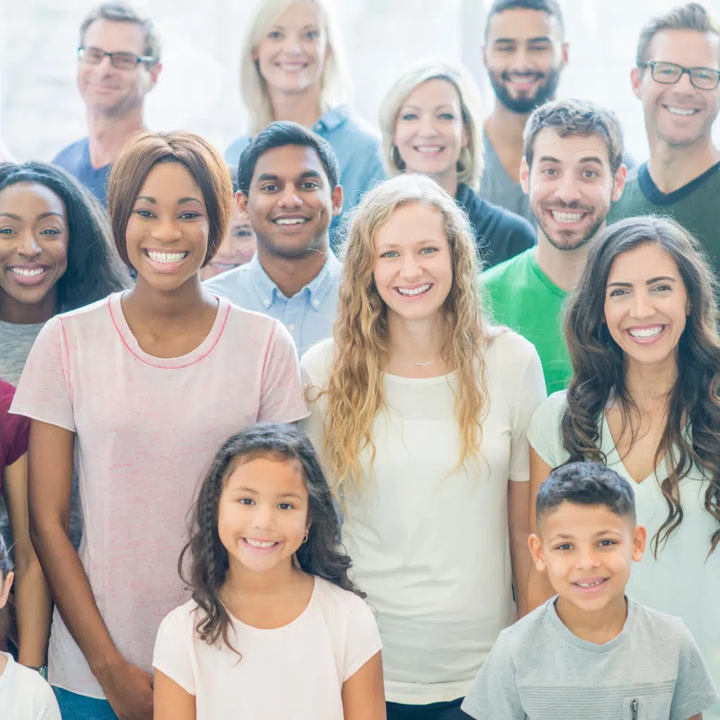Diverse group of smiling people of different ages standing together indoors.