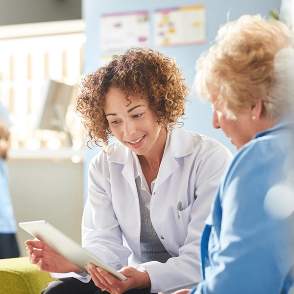 Pharmacist in white coat explaining information on a tablet to an elderly woman.