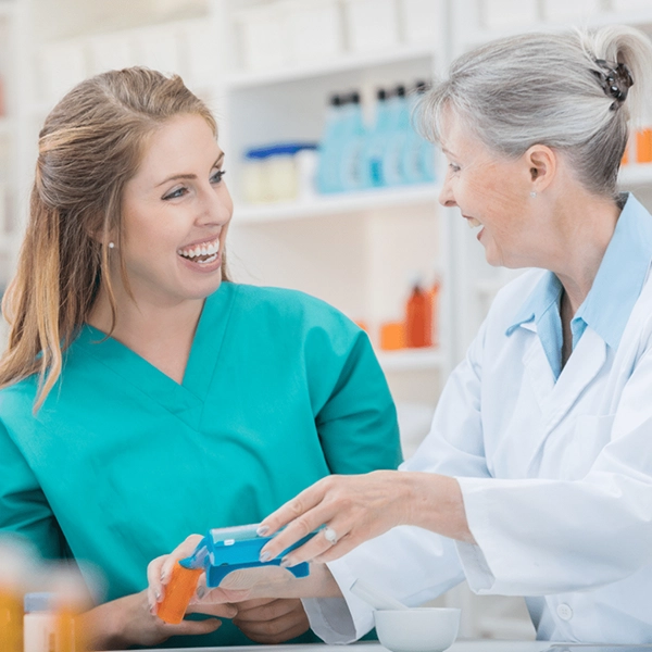 Two female healthcare professionals smiling and holding a pill bottle and medication organizer.