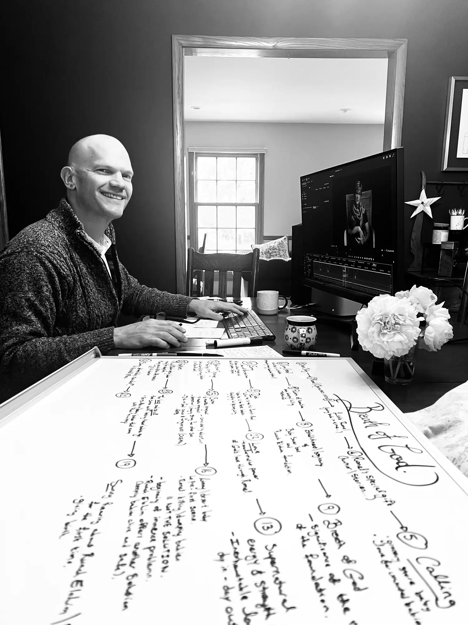 Noah Von Seydlitz-Riemer editing Breath of God at his desk beside a whiteboard mapping the film's story structure
