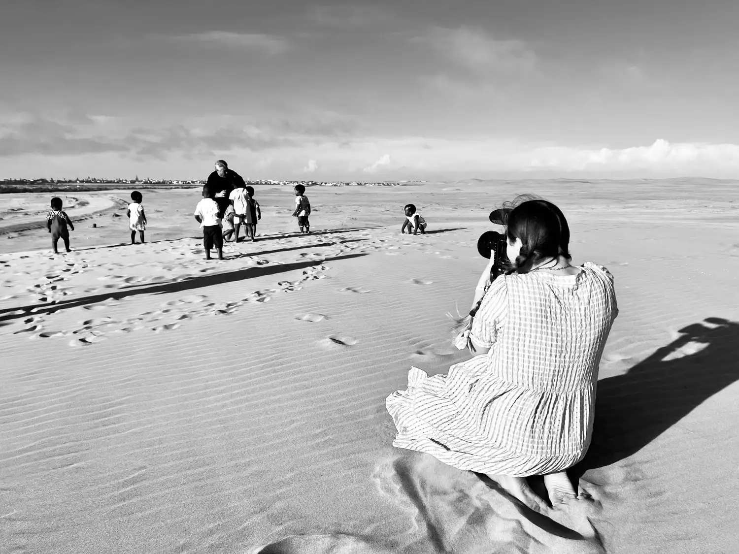 A filmmaker sitting on a sand dune watching children play during a shoot in Namibia