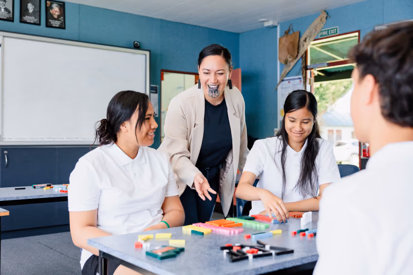 Teacher engaging with three students seated at a table with colorful learning blocks in a classroom.