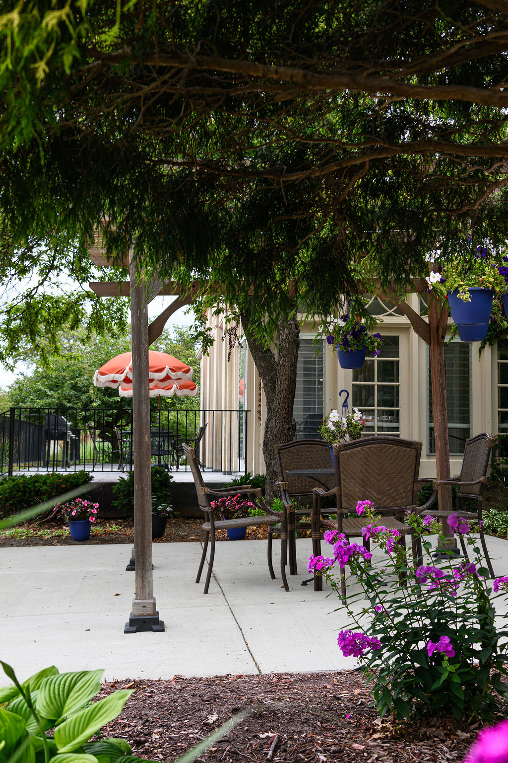 Outdoor patio with brown wicker chairs, hanging flower pots, and an orange umbrella in the background.