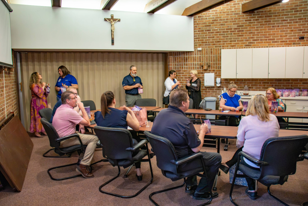 People socializing and sitting at tables in a room with brick walls and a crucifix on the wall.