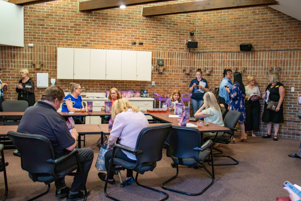 Group of people sitting and chatting in a brick-walled room with tables and chairs.