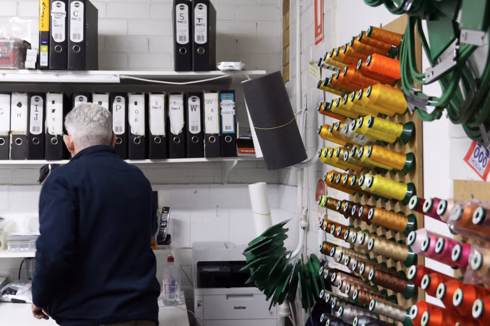 Uniforms Plus owner, Richard Innis, faces away while working on customer orders, he is surrounded by order folders and thread
