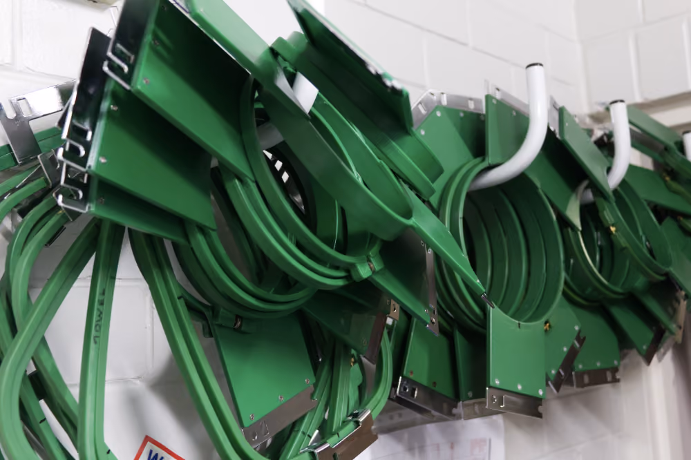 A wall with many green tajima embroidery hoops piled on hooks