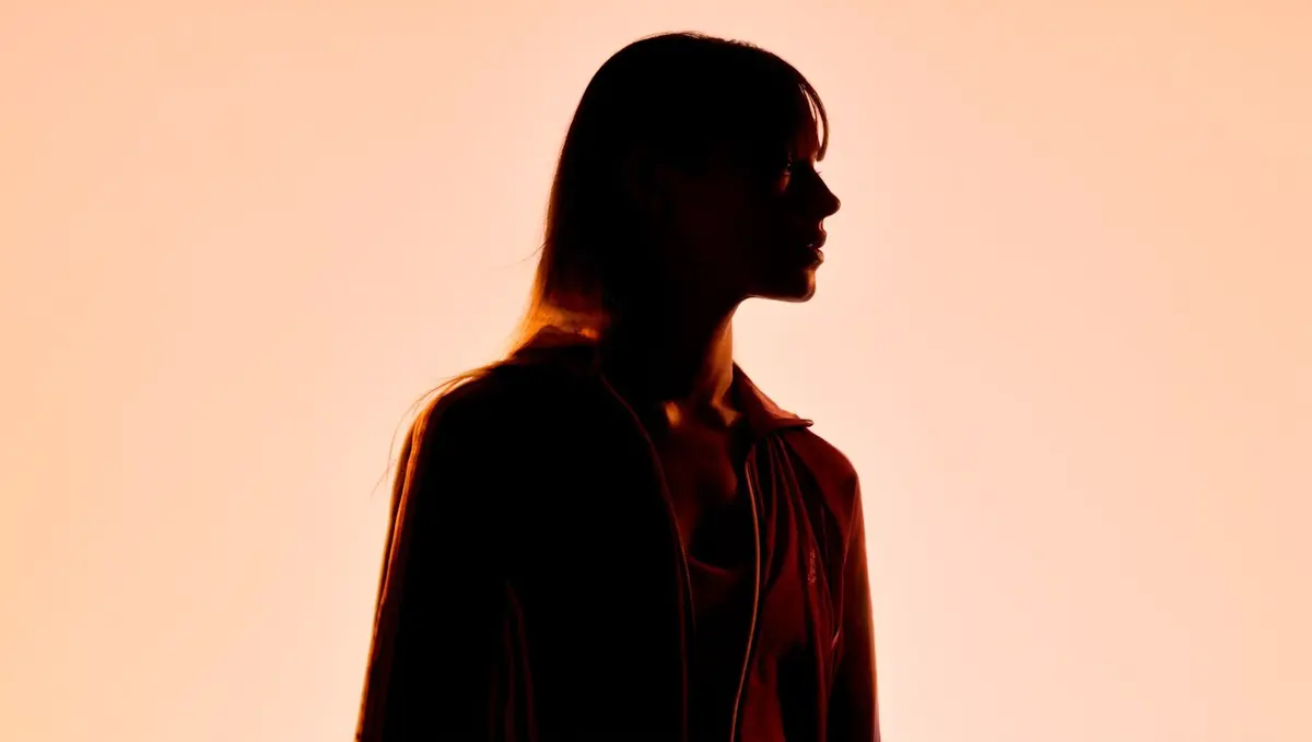 Silhouette of a person with long hair against a warm orange glowing background.