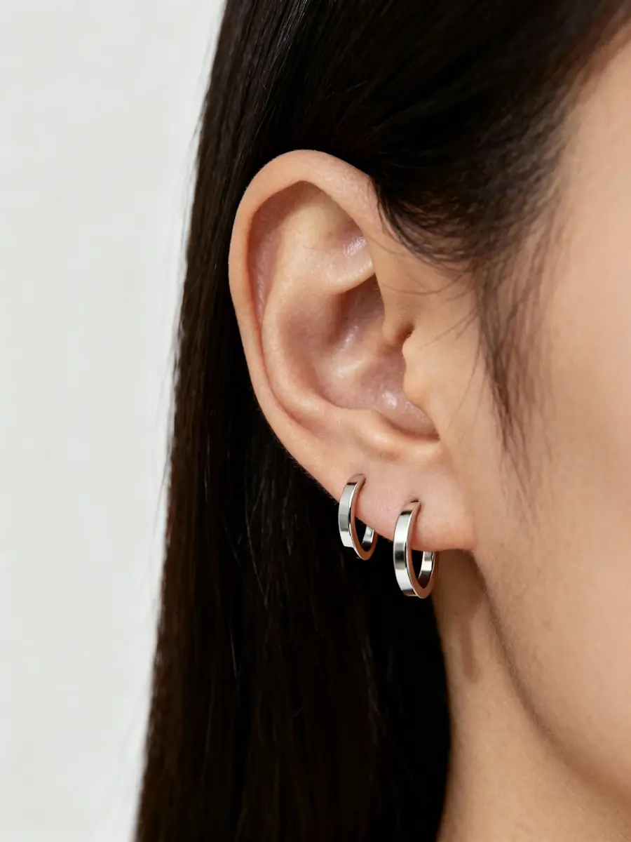 Close-up of an ear wearing two small silver hoop earrings of different sizes.