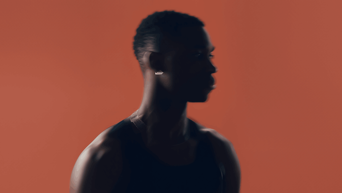 Silhouette of a man wearing a sleeveless top and necklace, set against a solid reddish background.