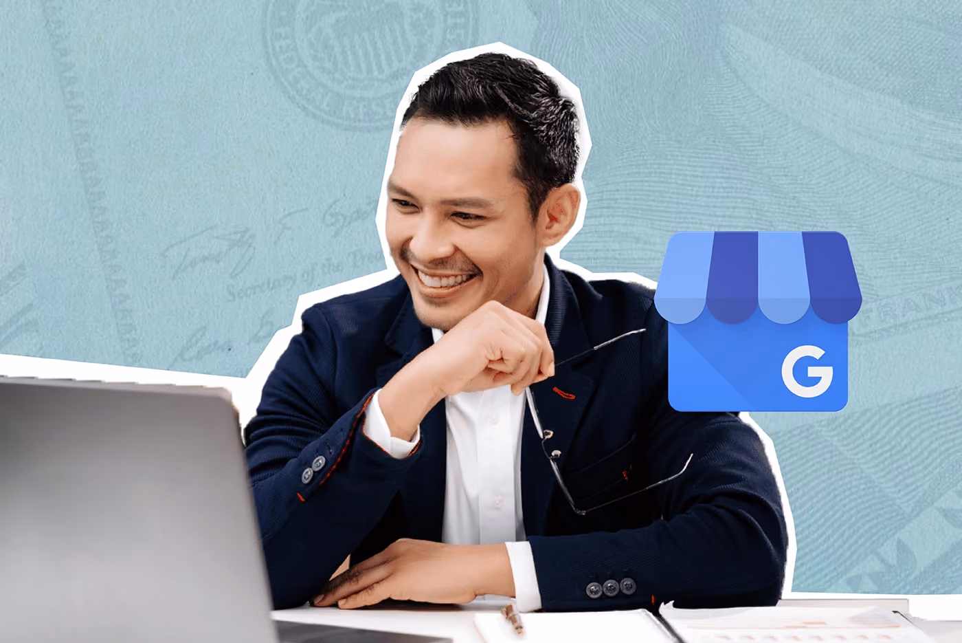 Asian man wearing suit sits at desk and smiles at open laptop.