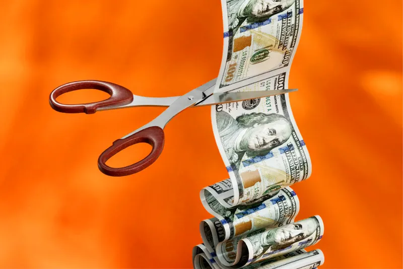 Scissors cutting printed dollar bills