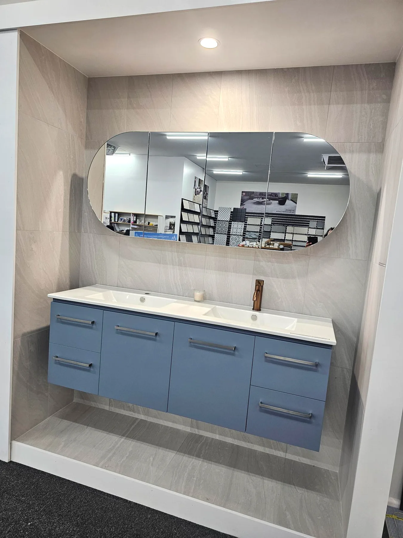 Showroom display bay with a dusty blue wall hung double vanity and oval mirror cabinet