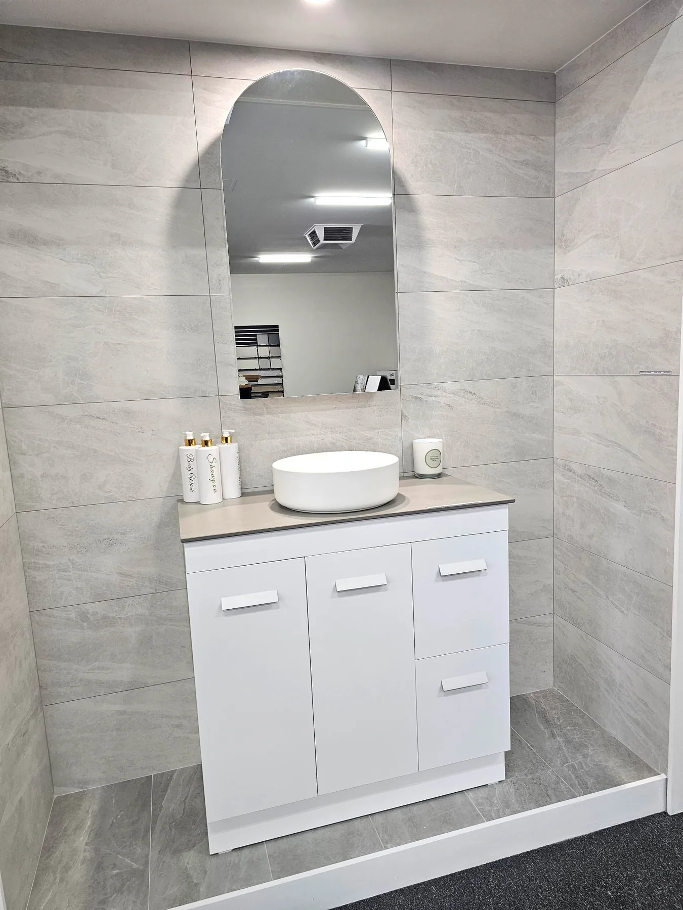 White freestanding vanity with grey stone top, round vessel basin and frameless arched mirror