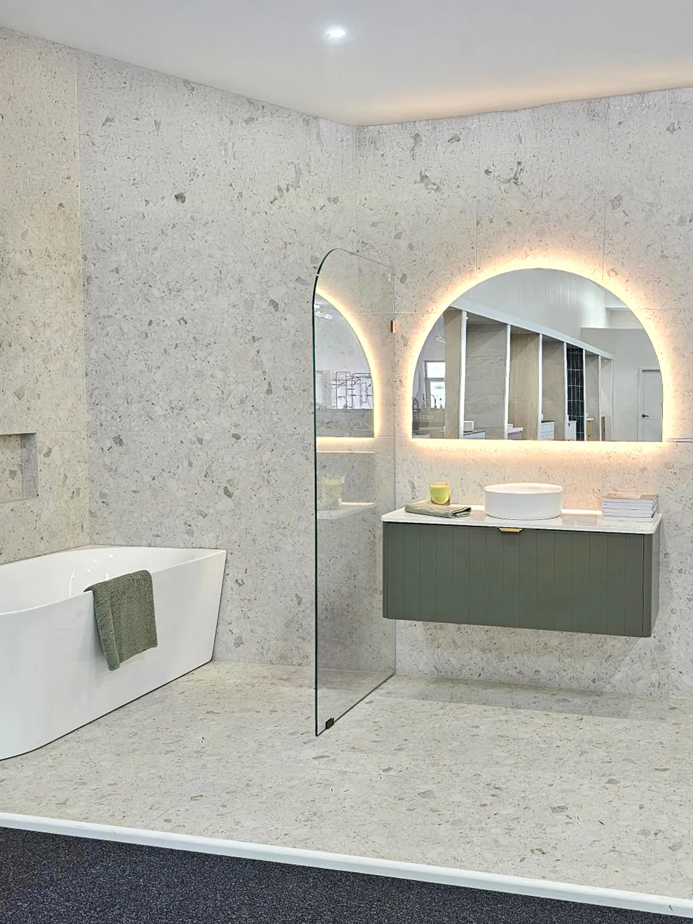 Olive fluted wall hung vanity, arched backlit mirror and freestanding bath against terrazzo look tiles