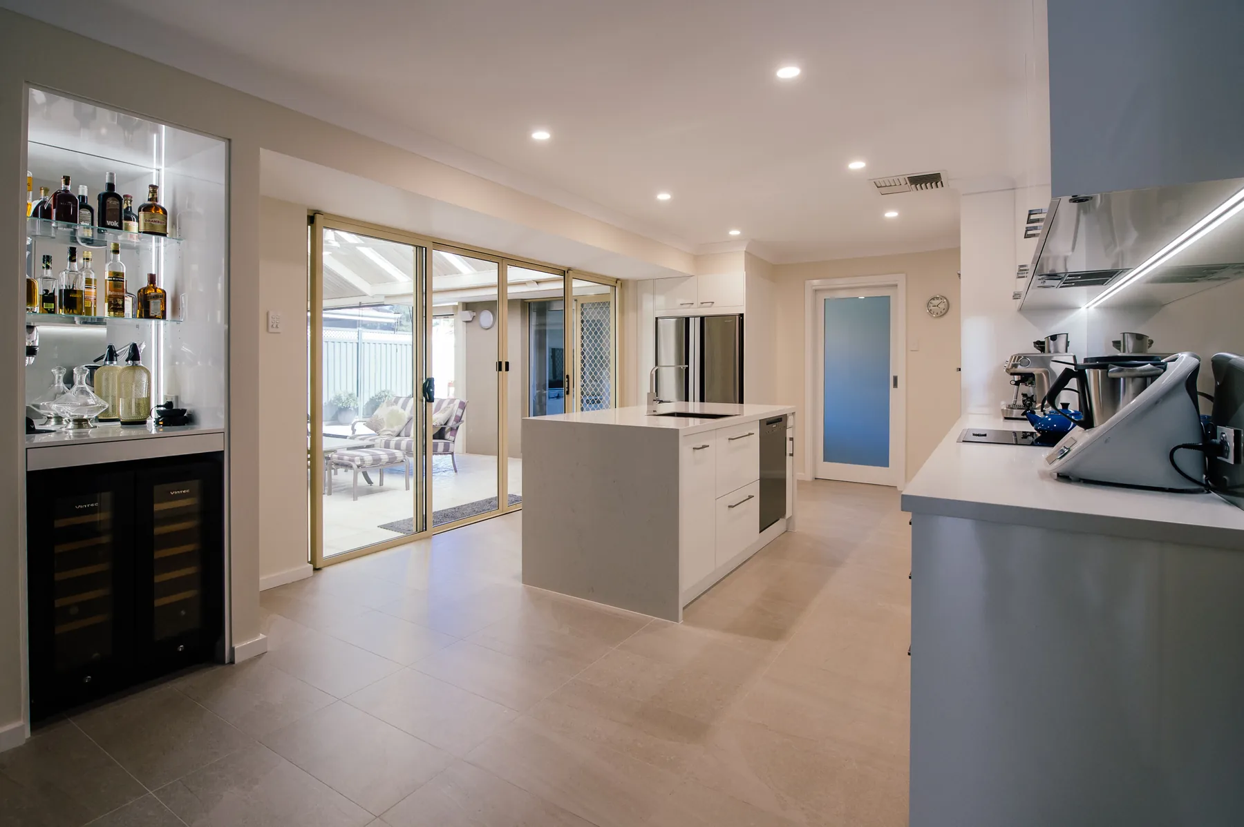 Completed kitchen renovation with white stone island bench, wine fridge and large format floor tiles
