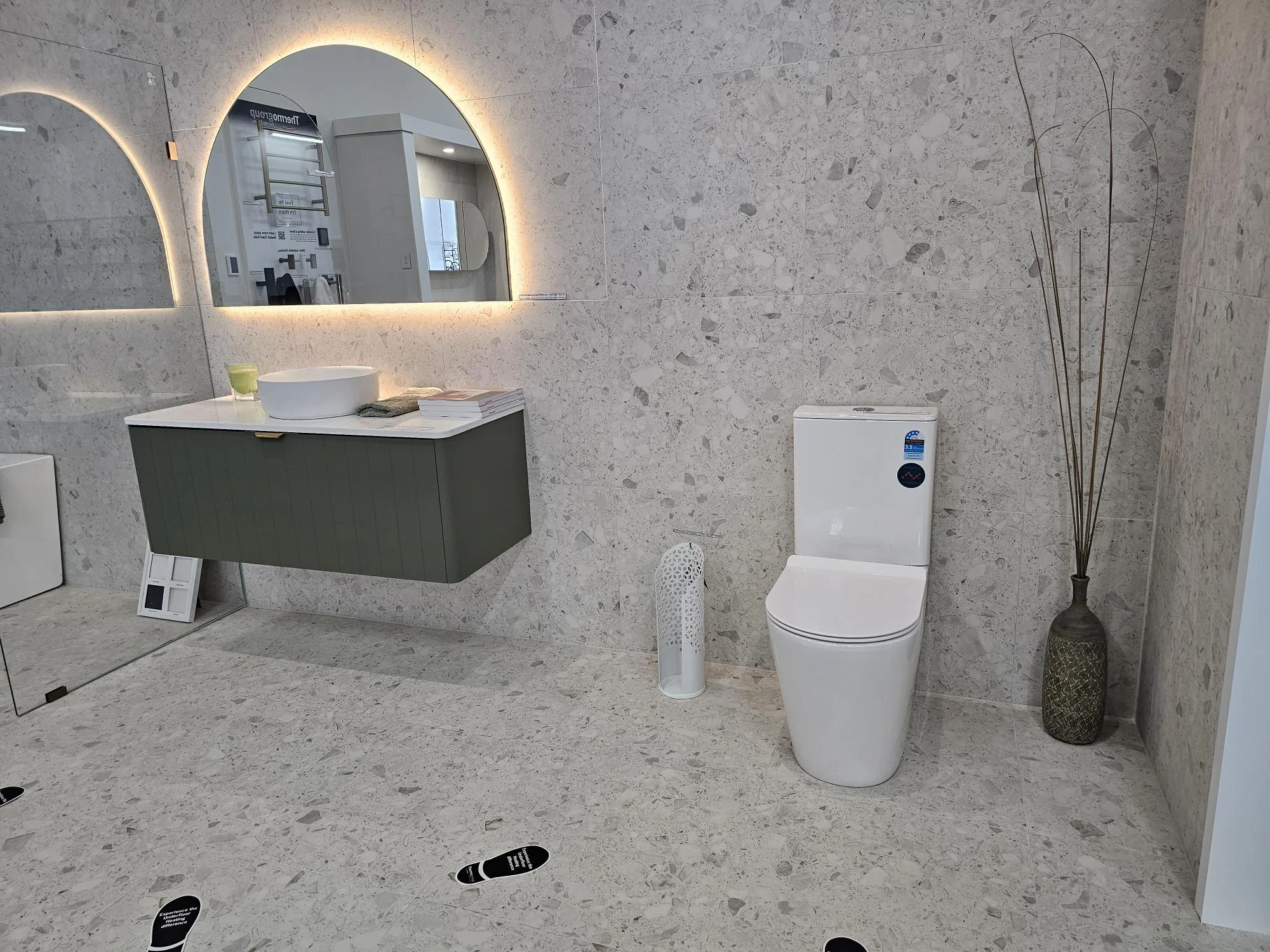 A styled bay with an olive wall hung vanity, arched backlit mirror and a back to wall toilet suite