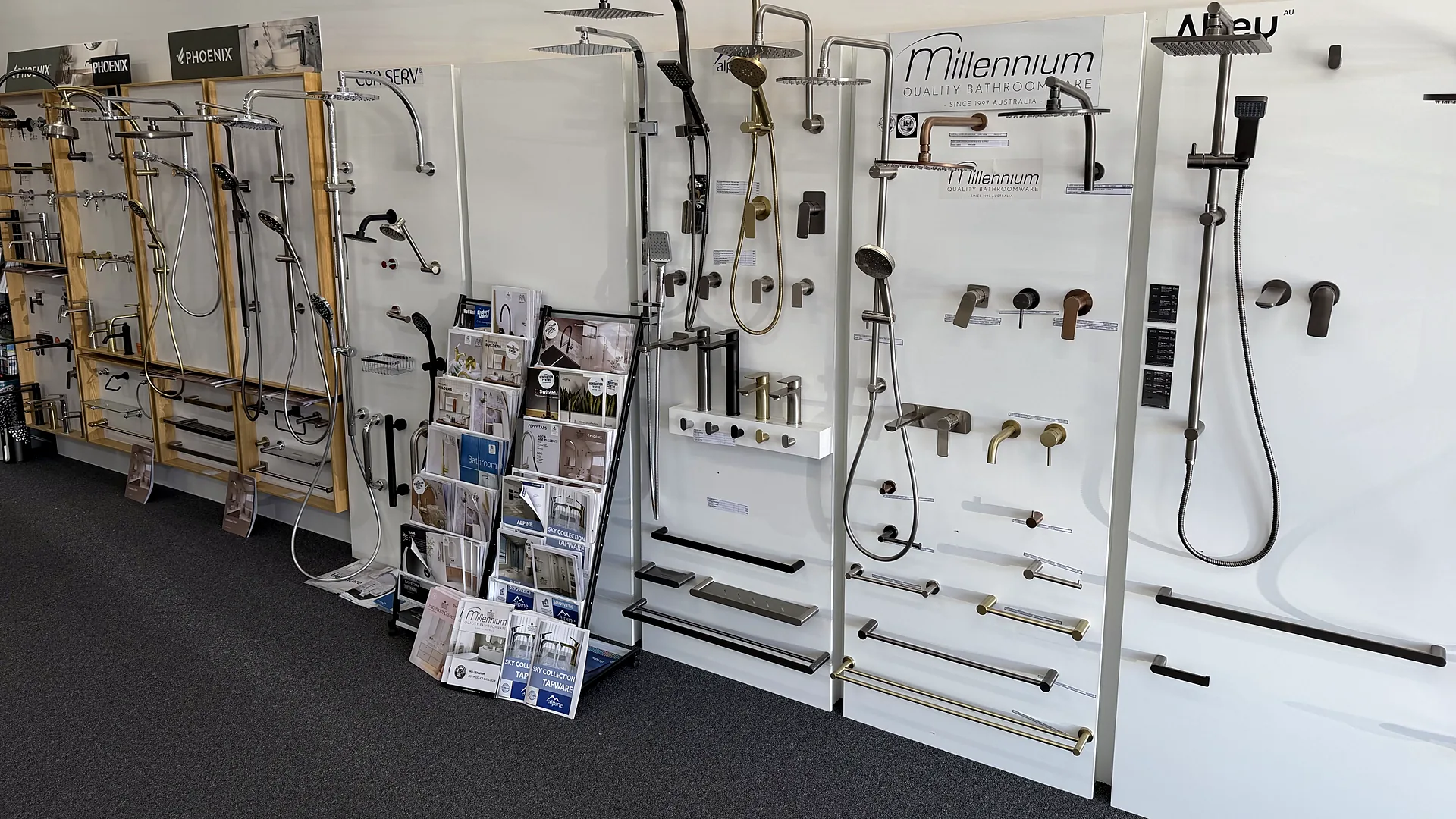 Millennium Quality Bathroomware display panel with rain showers, a hand shower on a rail and wall mixers in brushed brass, gunmetal and matte black