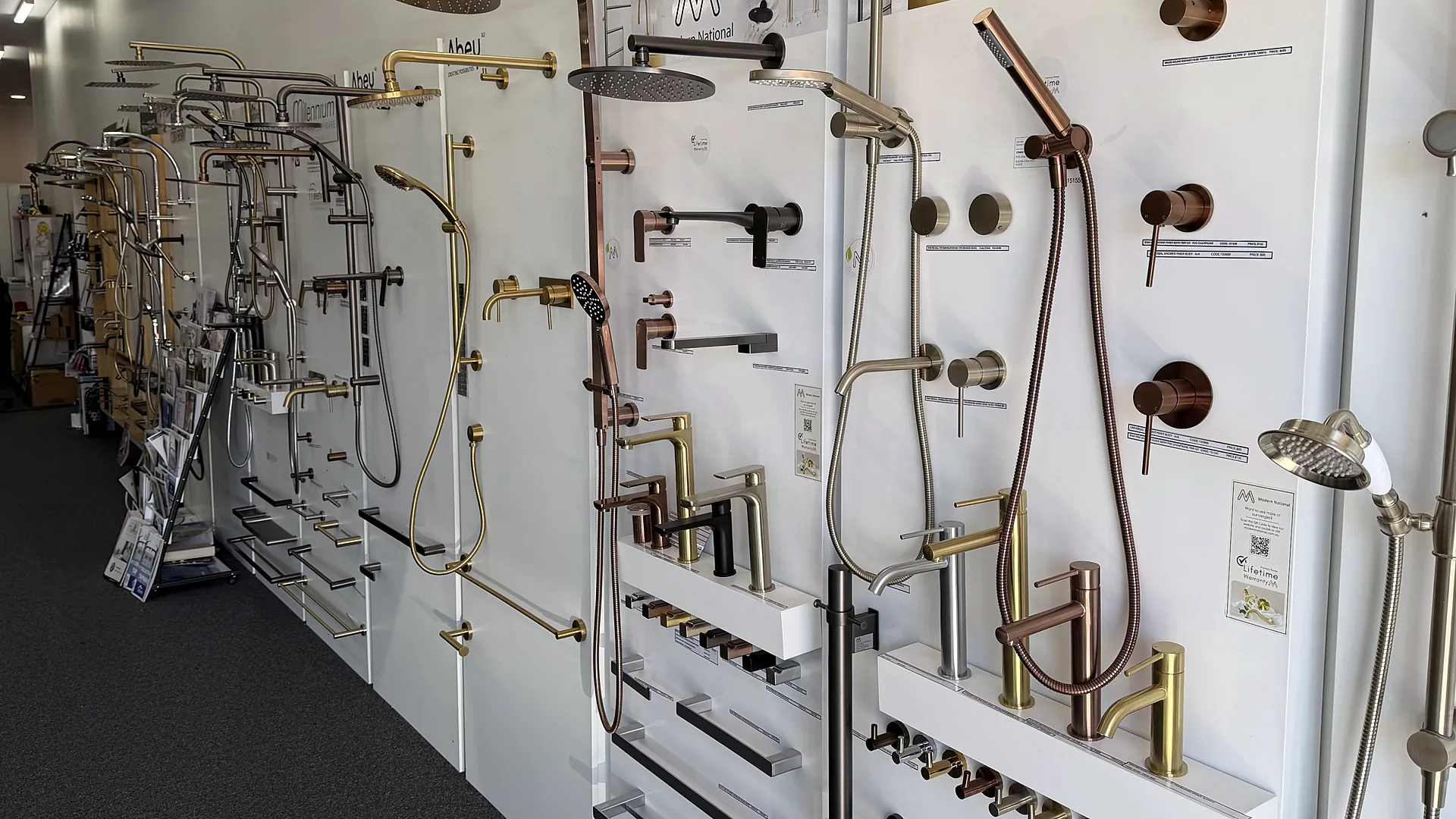 Shower and tapware display wall in the Osborne Park showroom with rain showers, hand showers on rails and wall mixers in copper, brushed brass and matte black