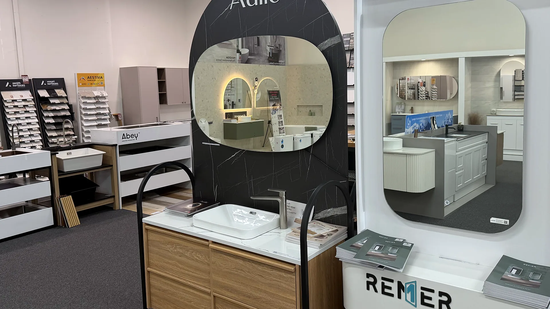 Showroom bay with a black marble look feature panel, arched and rounded mirrors, a timber vanity with a stone basin, and stone and tile sample racks alongside