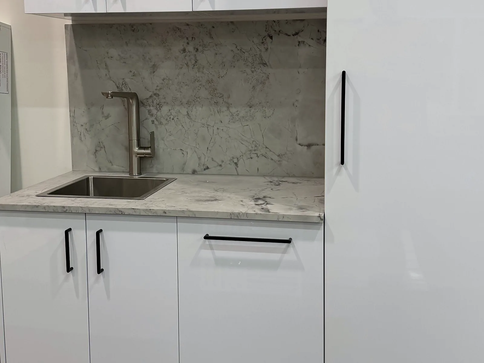 Laundry run with gloss white cabinetry, matte black bar handles, a marble look benchtop and splashback and a stainless undermount trough