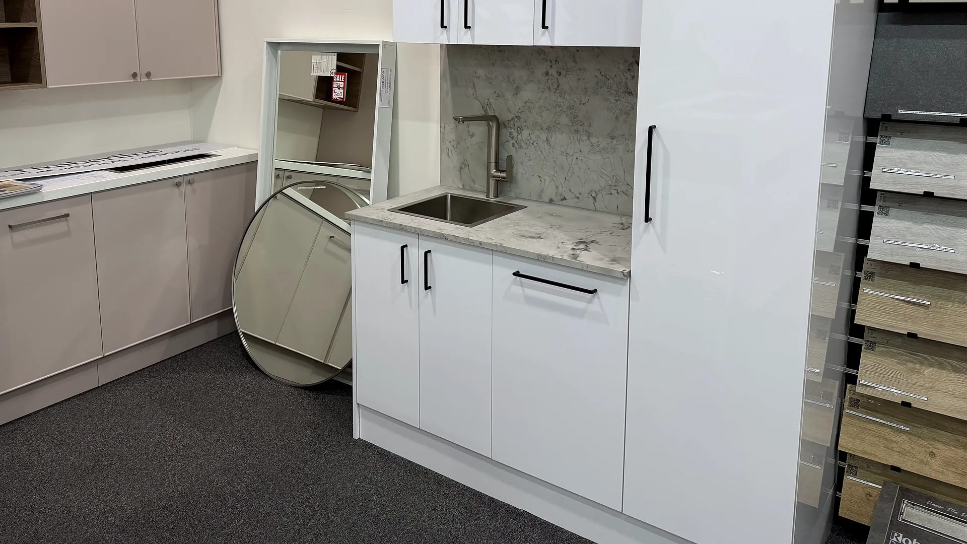 Timberline modular laundry on display in Osborne Park with gloss white cabinetry, a marble look benchtop and splashback, an undermount stainless trough and taupe overhead cupboards