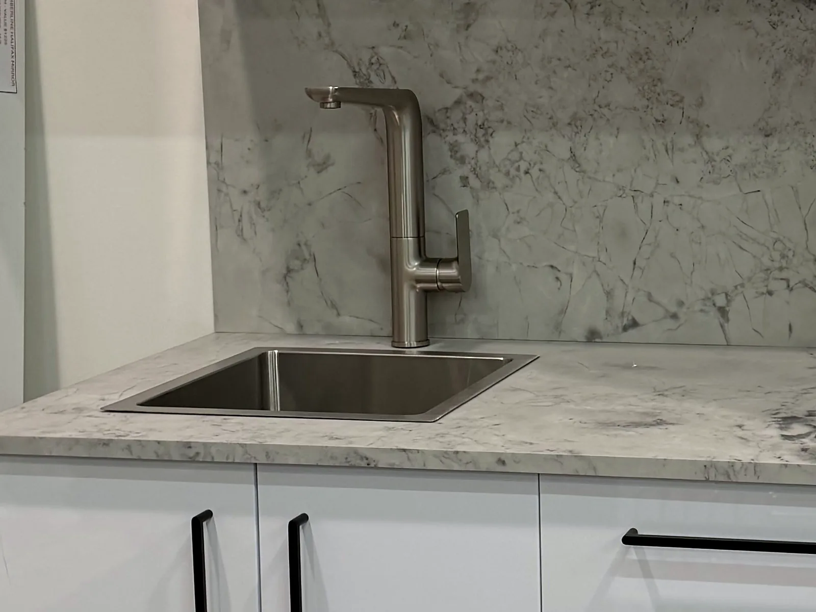 Undermount stainless steel laundry trough set into a marble look benchtop with a brushed nickel pull out mixer