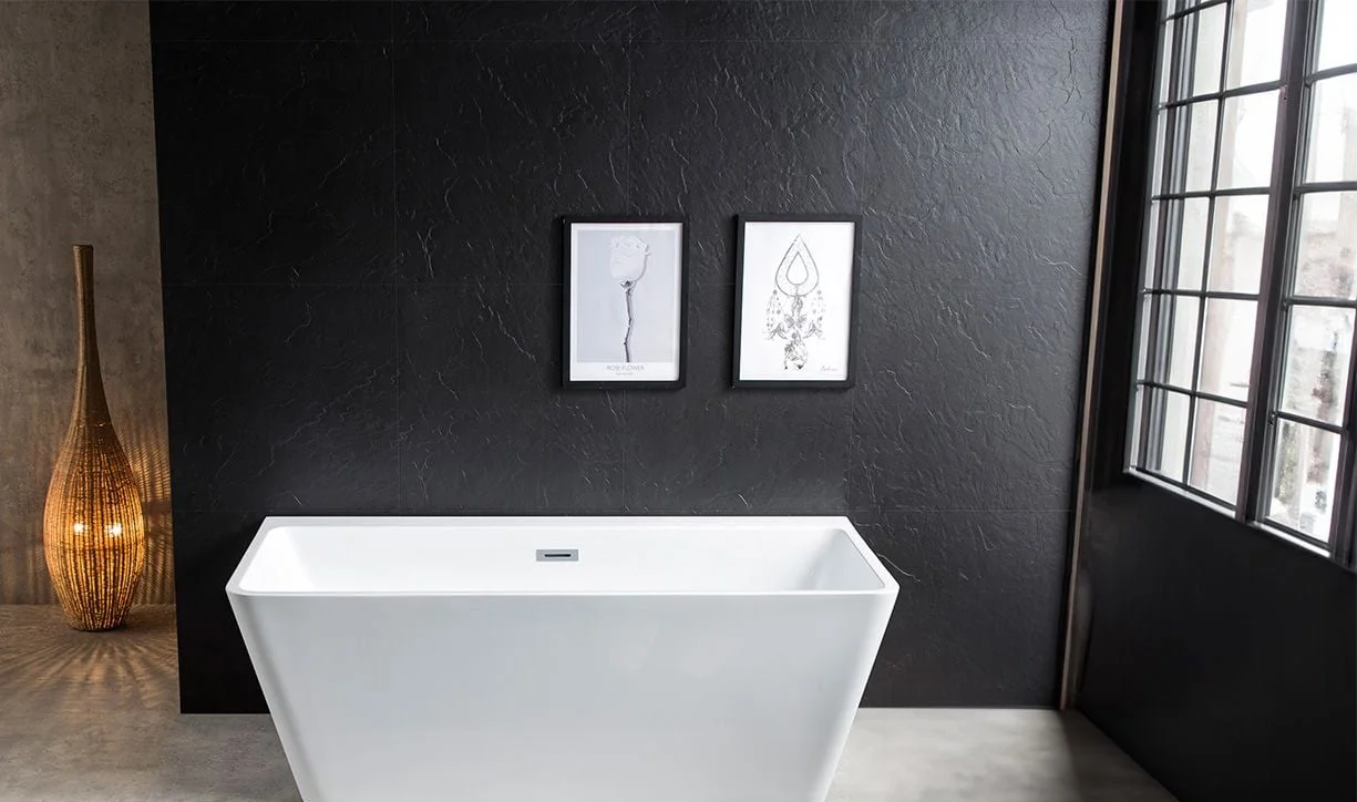 Square edge freestanding bath styled against a matte charcoal feature wall with a warm stone floor and a black framed window