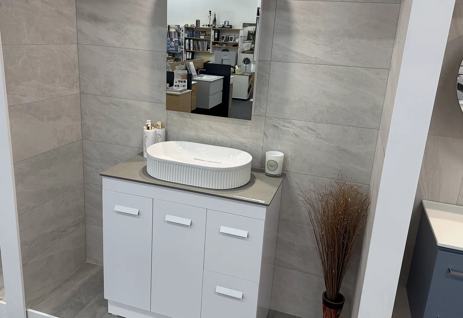 Showroom bay tiled floor to wall in large format grey stone look porcelain, with a white floor standing vanity and a fluted oval basin