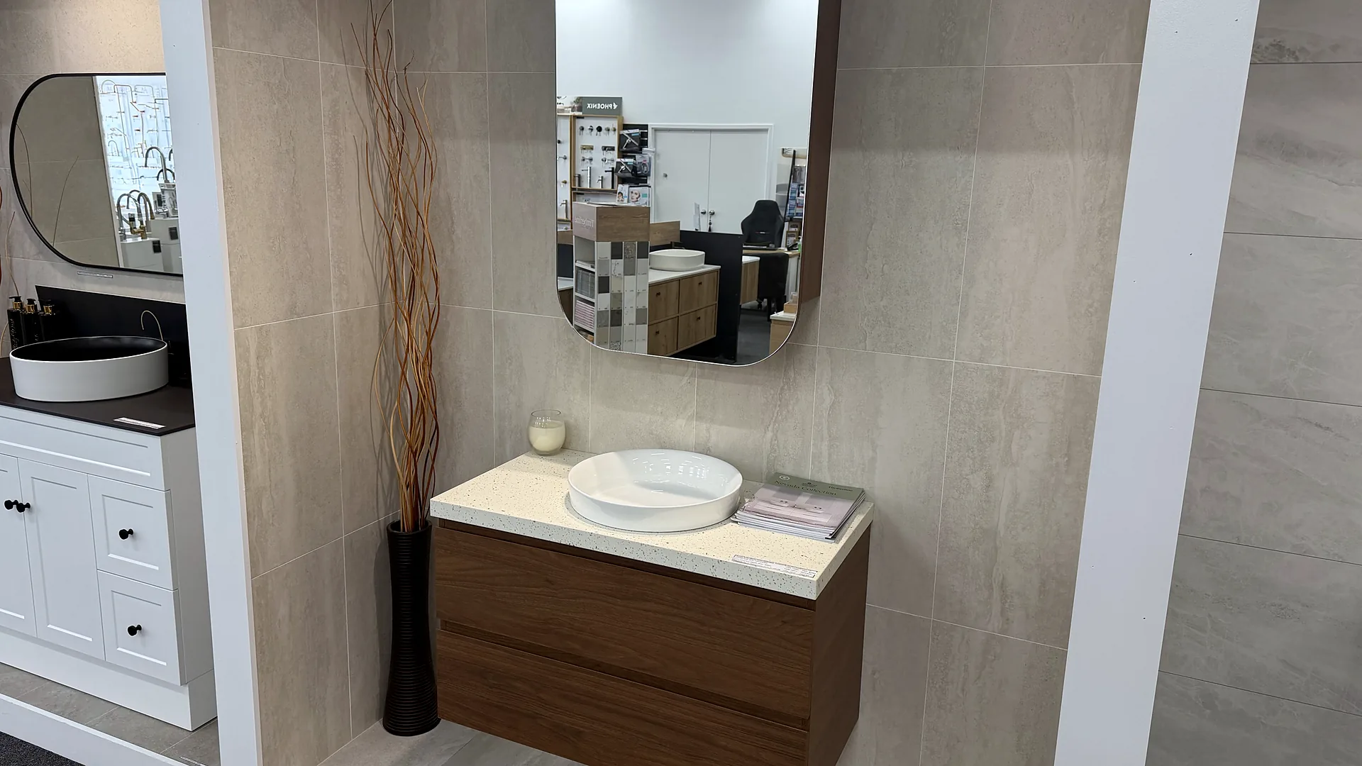 Walnut timber wall hung vanity with a stone top and a stone basin under a rectangular mirror, in a large format tiled display bay