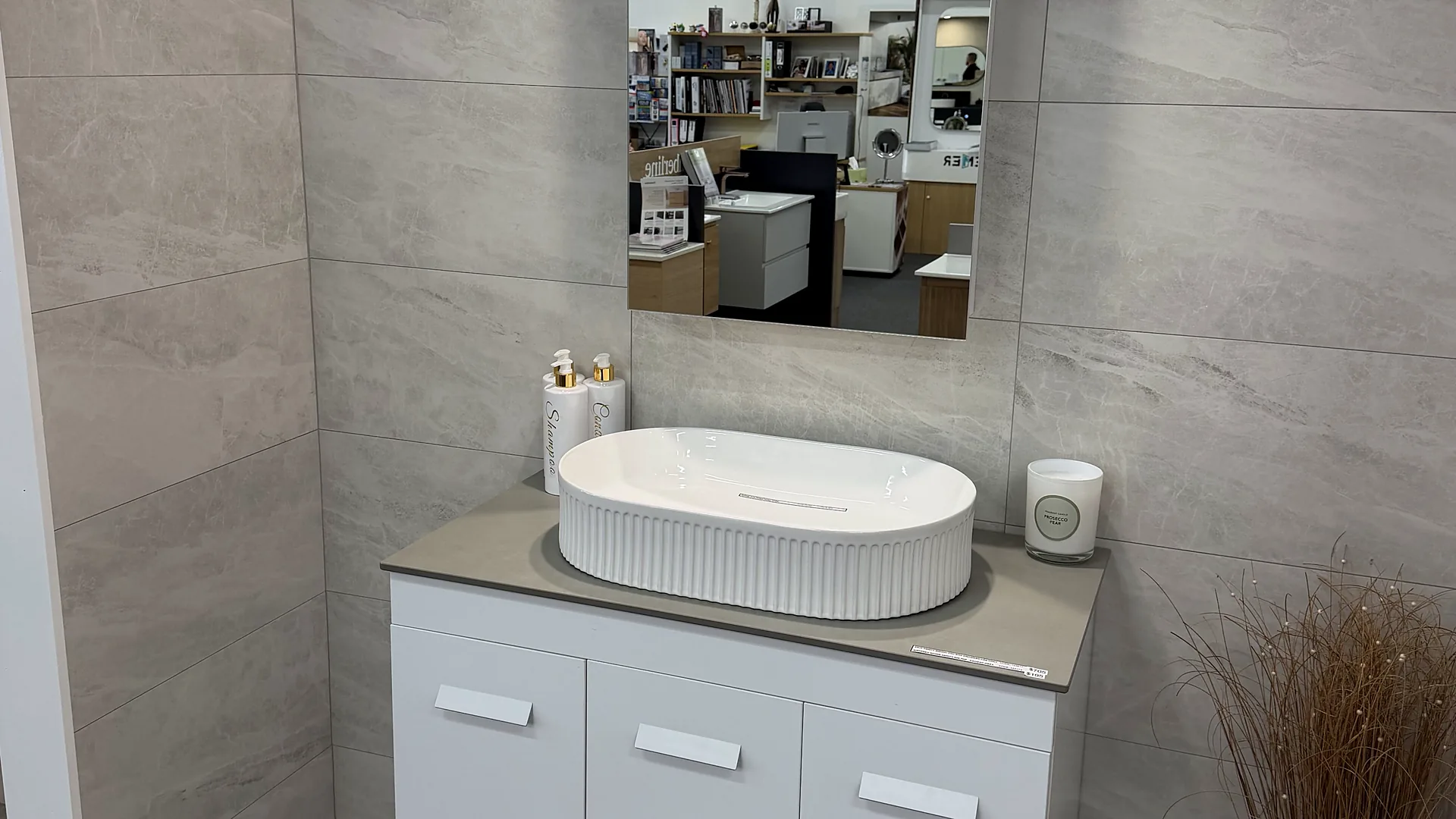 Showroom bay tiled in large format stone look porcelain, with a white vanity, a stone benchtop and a fluted oval basin