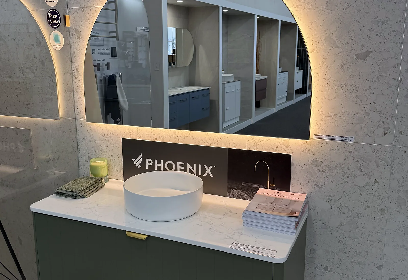 Arched backlit mirror above an olive green wall hung vanity with a stone benchtop and a round basin in the Osborne Park showroom