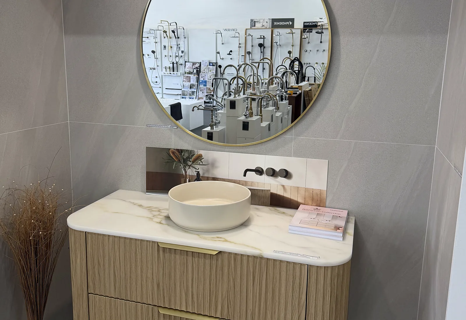 Fluted timber wall hung vanity with a marble look top, a round stone basin and a gold rimmed circular mirror in the Osborne Park showroom