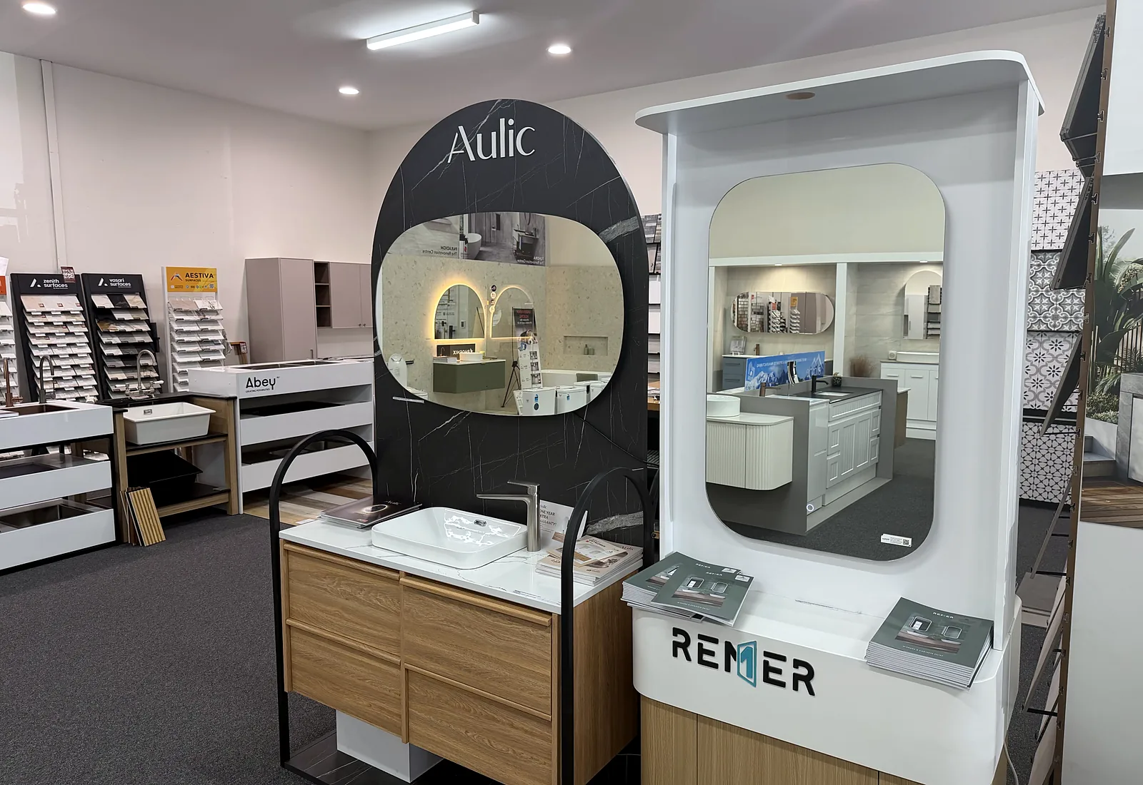 Arched Aulic display bays in the Osborne Park showroom with backlit mirrors, timber vanities and stone basins, with sample racks alongside