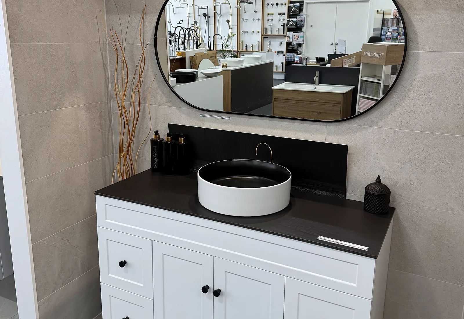 White shaker vanity with a dark stone benchtop, a matte black round vessel basin and an oval mirror in the Osborne Park showroom