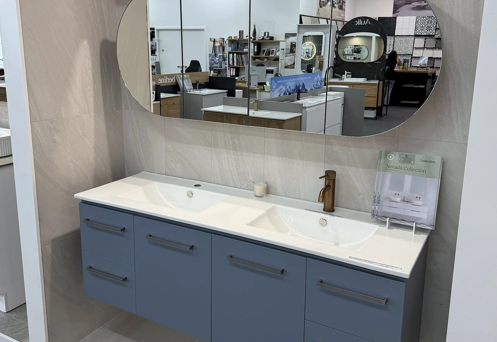 Dusty blue wall hung double vanity with a moulded twin basin top, a brushed brass mixer and an oval mirror cabinet in the Osborne Park showroom