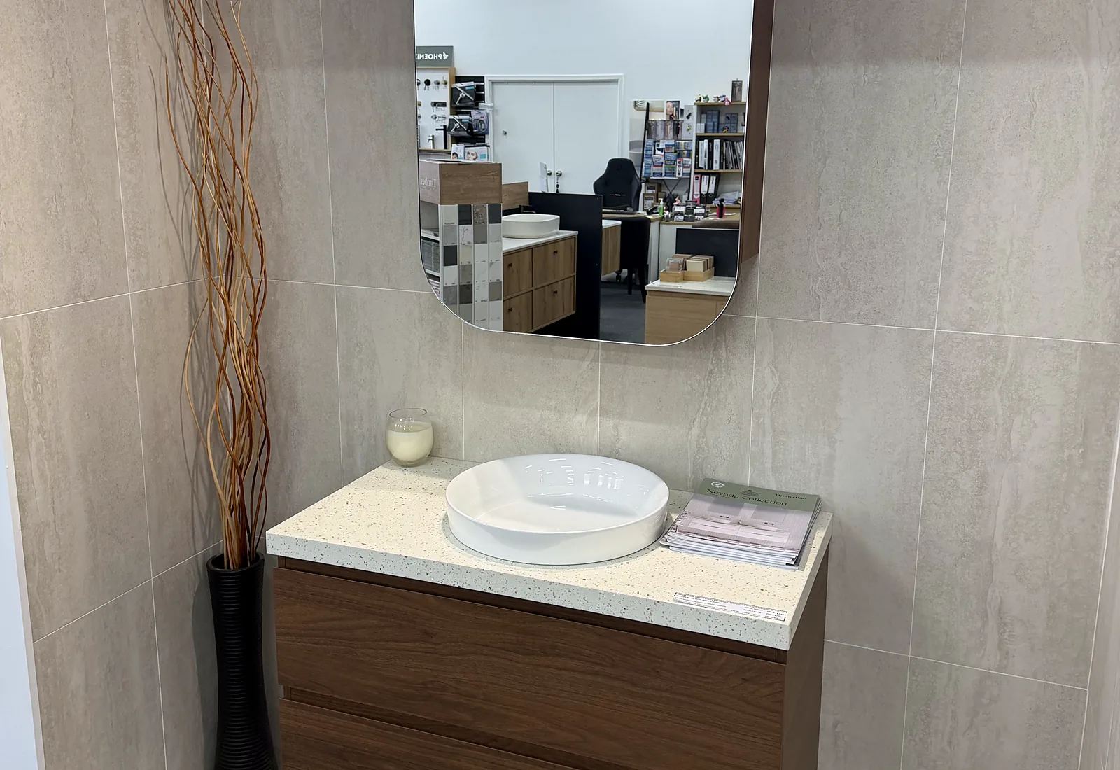 Walnut wall hung vanity with a speckled stone top, an oval basin and a soft edged mirror in a large format tiled display bay