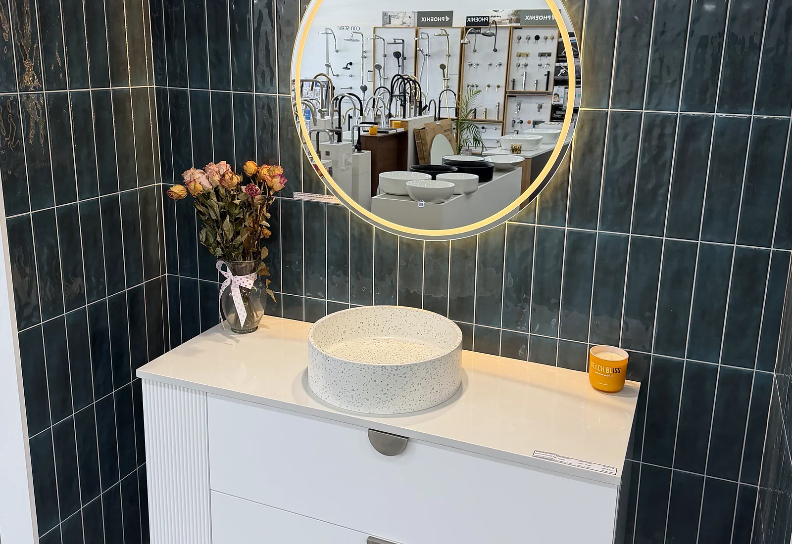 Deep green vertical tiled feature wall with a backlit round mirror, a white fluted vanity and a speckled terrazzo basin in the Osborne Park showroom
