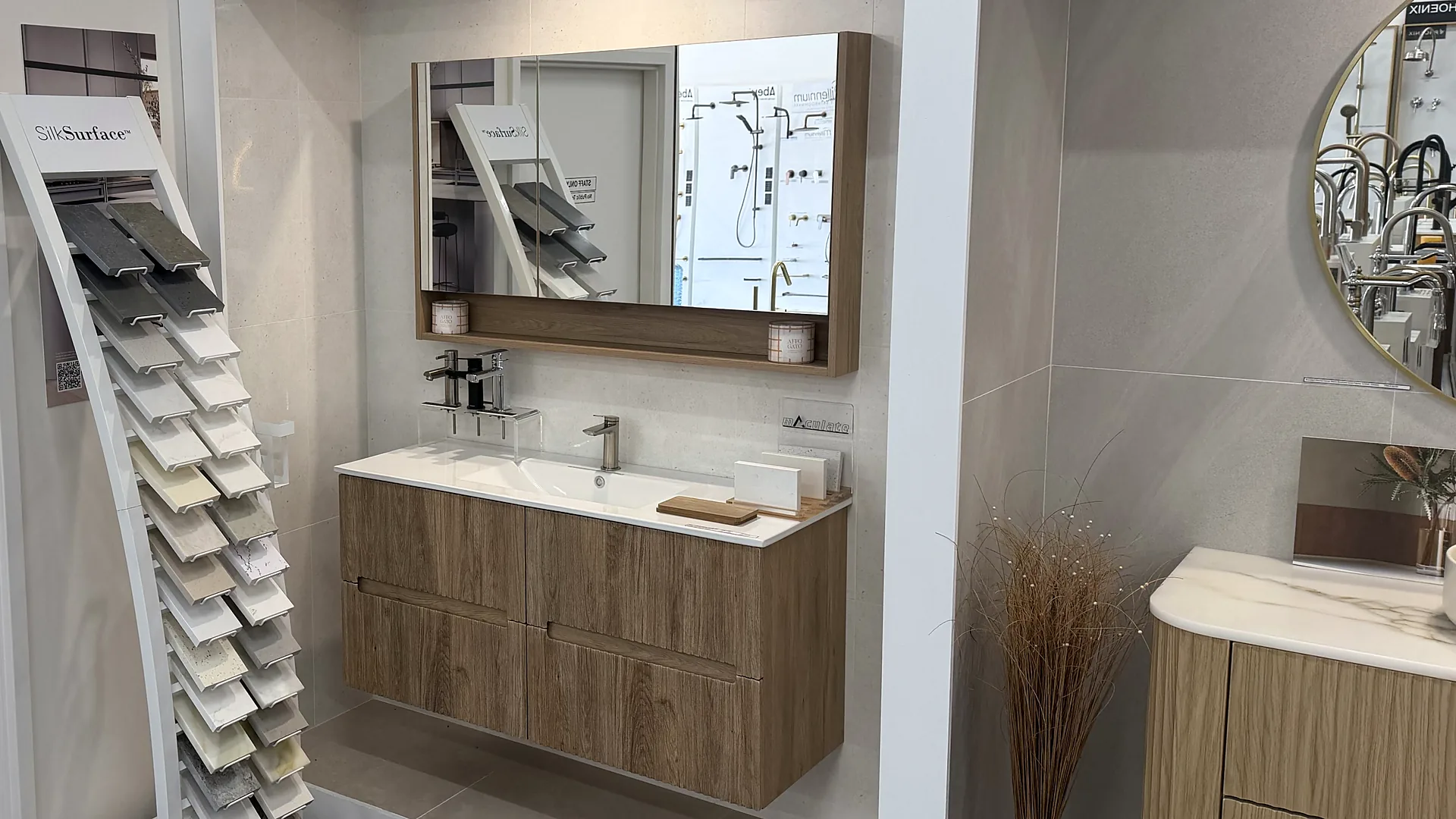 Timber wall hung vanity with a moulded basin top and a timber mirror cabinet in a large format tiled bay, with a stone surface sample rack alongside