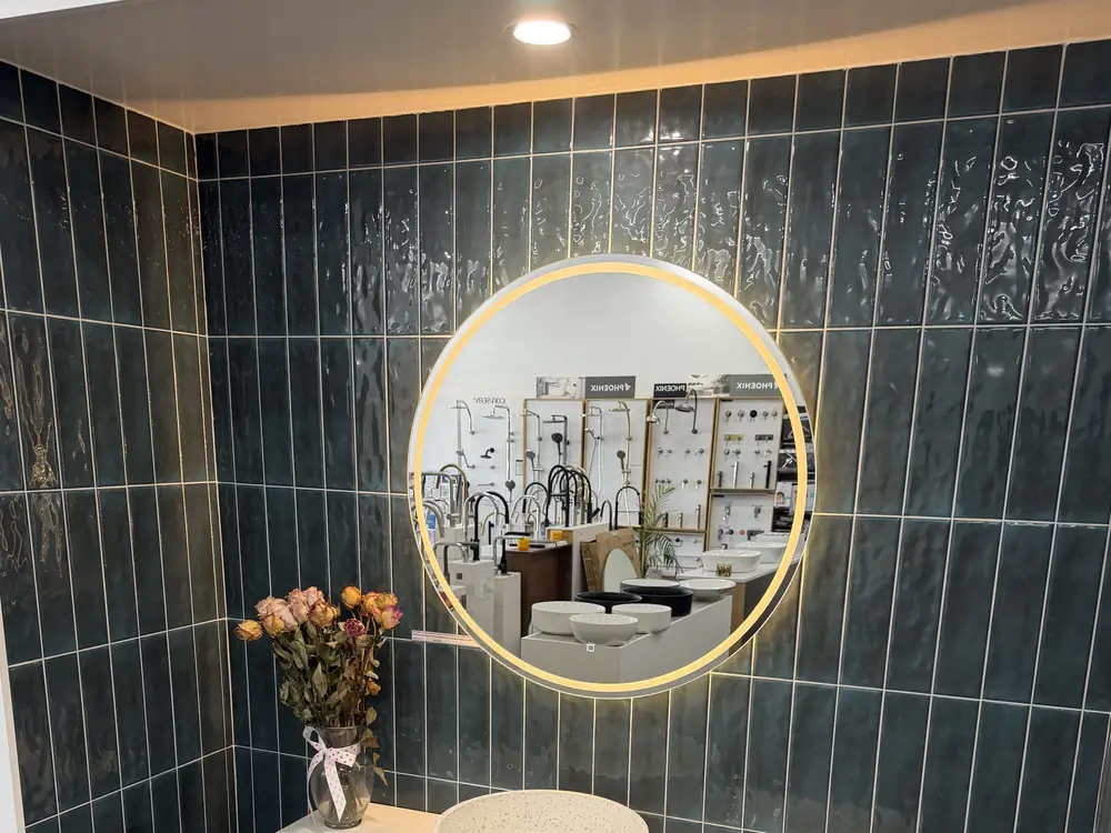 Deep teal gloss vertical wall tiles in a display bay at the Osborne Park showroom, with a round backlit mirror and large format grey floor tile