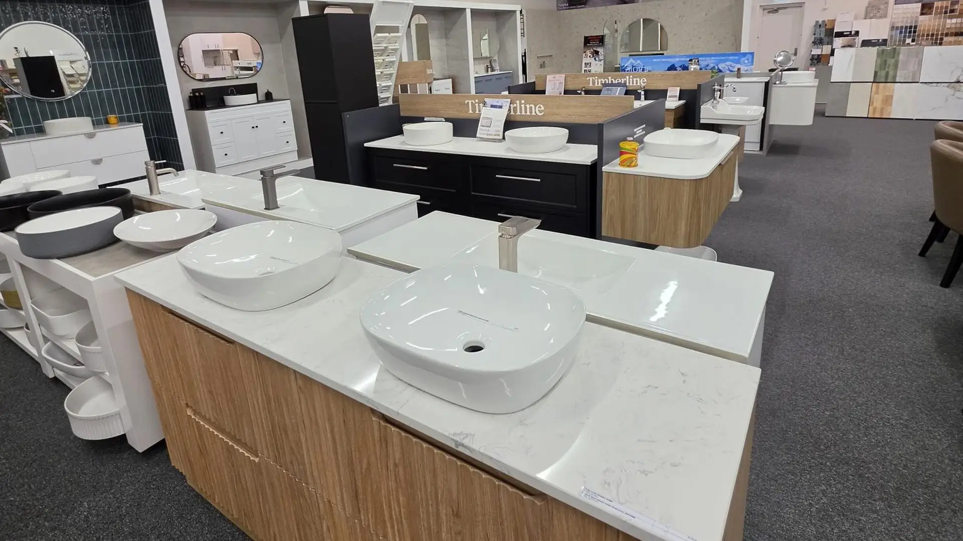 Vanity display island in the Osborne Park showroom with white above counter basins on a marble look stone top, a timber drawer vanity and Timberline signage behind